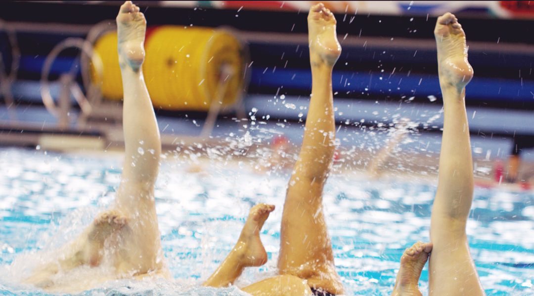 Swimmers in pool with their legs pointing up above the water